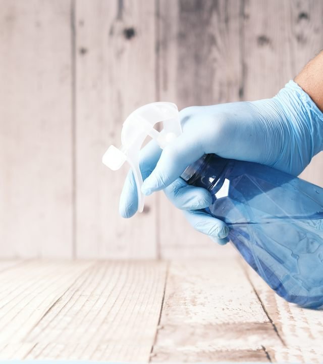 Cleaner in protective gloves sanitising a surface